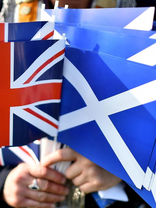 Eine Person hält mehrere Papierflaggen in der Hand. Sowohl welche mit Schottlands Wappen als auch dem Union Jack.
