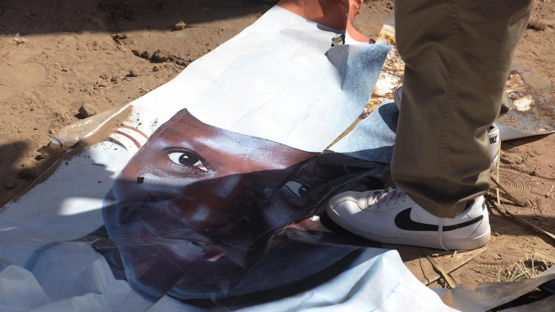 Ein Fuß steht auf dem am Boden liegenden Wahlplakat des abgewählten gambischen Präsidenten Jammeh.