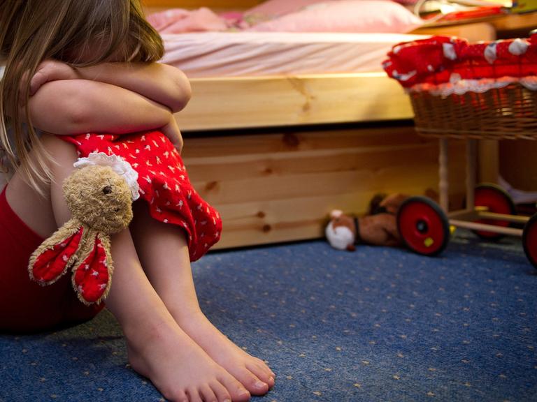 Ein kleines Mädchen sitzt weinend auf dem Fußboden in seinem Zimmer.
