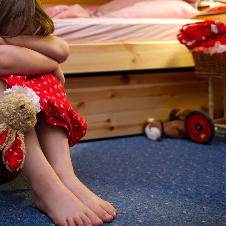 Ein kleines Mädchen sitzt weinend auf dem Fußboden in seinem Zimmer.