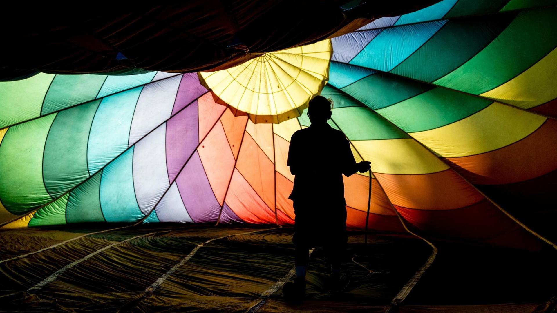 Ein Mann steht unter einem Heißluftballon in regenbogenfarben.