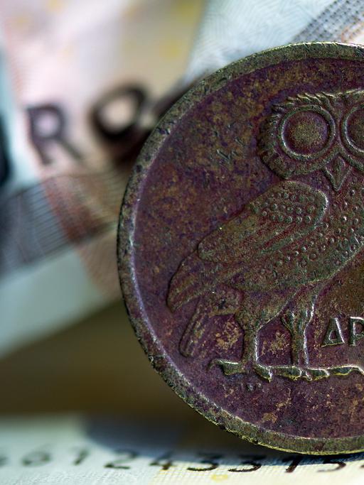 Eine griechische Drachmenmünze liegt auf geknüllten Euroscheinen.