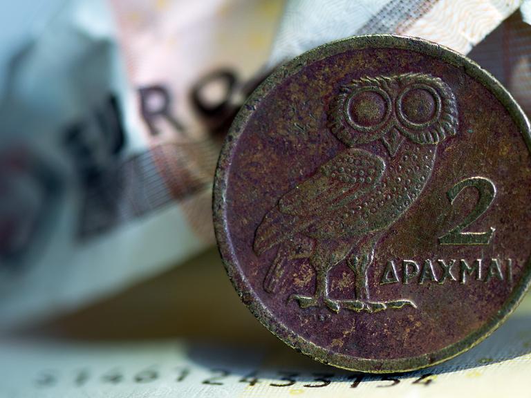 Eine griechische Drachmenmünze liegt auf geknüllten Euroscheinen.