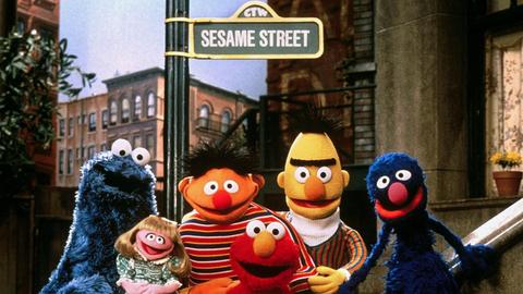 Die Puppen der Kindersendung Sesamstraße, das Krümelmonster, Mariechen, Ernie, Elmo, Bert und Grobi stehen vor einem Straßenschild mit der Aufschrift "Sesame Street"