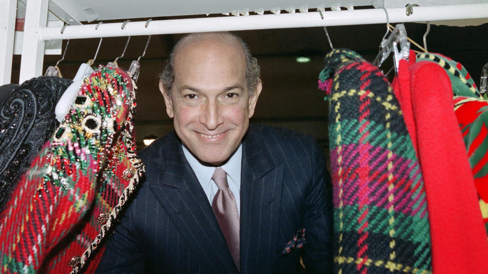 Der Designer schaut zwischen Mänteln hindurch, die auf einer Kleiderstange hängen.
