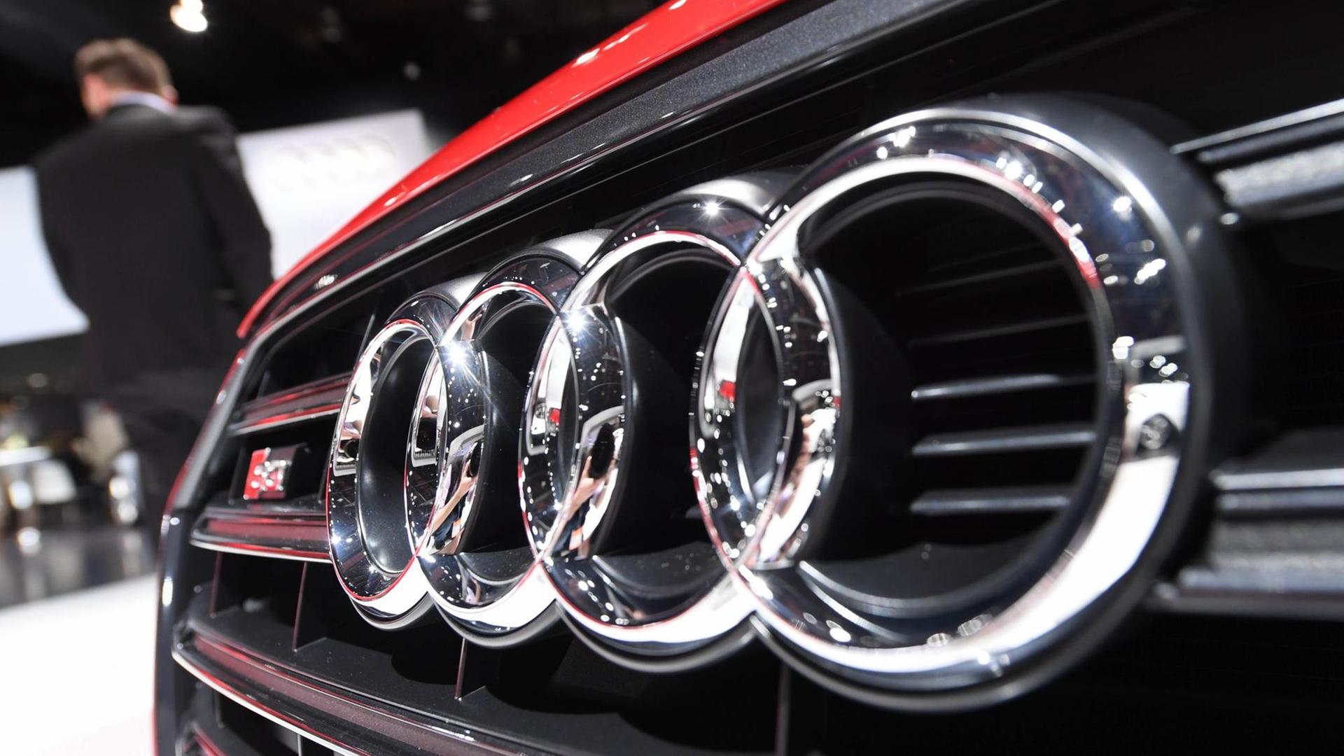 Das Logo von Audi mit seinen Kreisen auf der Frontschürze eines roten Autos.