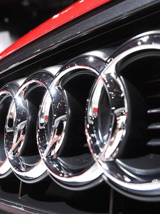 Das Logo von Audi mit seinen Kreisen auf der Frontschürze eines roten Autos.