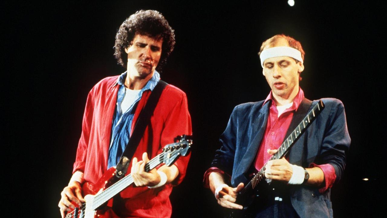 Der Sänger Mark Knopfler der bitischen Rockgruppe "Dire Straits"  mit Stirnband, rotem Hemd und Jackett und der Bassist John Illsley - dunkle Locken und rote Jacke - bei einem Auftritt in Helsinki/Finnland auf der Bühne (Aufnahme vom 28.10.1985).
