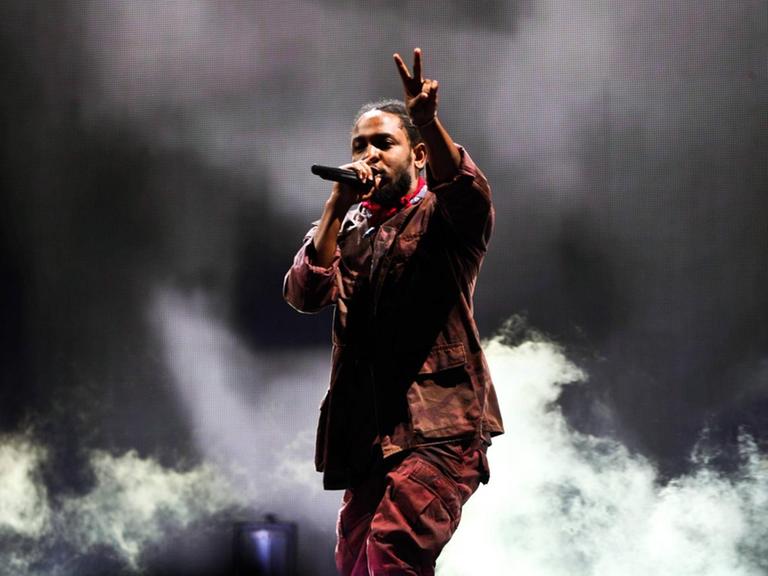 Kendrick Lamar beim Panorama Music Festival 2016 in New York. Der Musiker steht vor dunklem Hintergrund und macht mit einer Hand das Peace-Zeichen