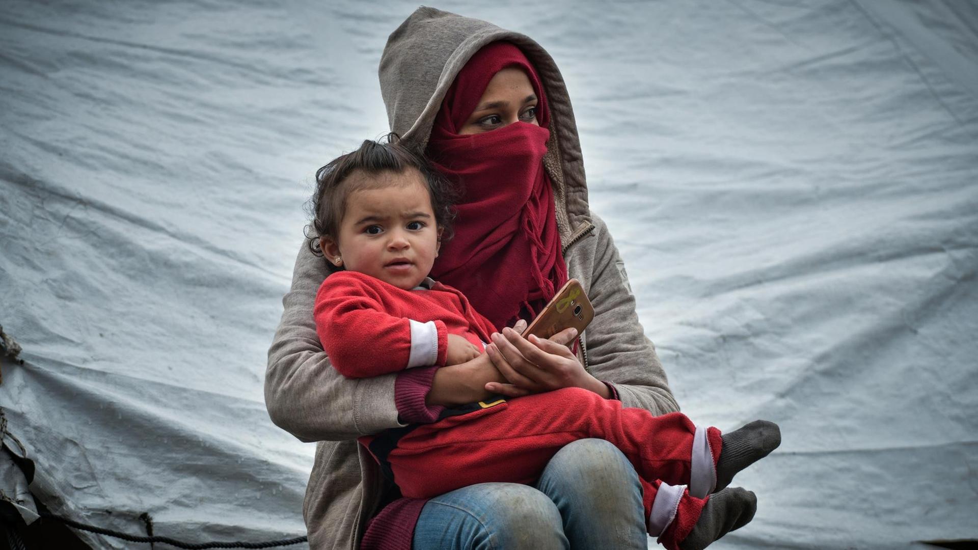 Momentaufnahme aus dem Flüchtlingslager Moria auf der Insel Lesbos am 10.03.2020. Zu sehen ist eine junge Frau, die ein kleines Kind im Arm hält.