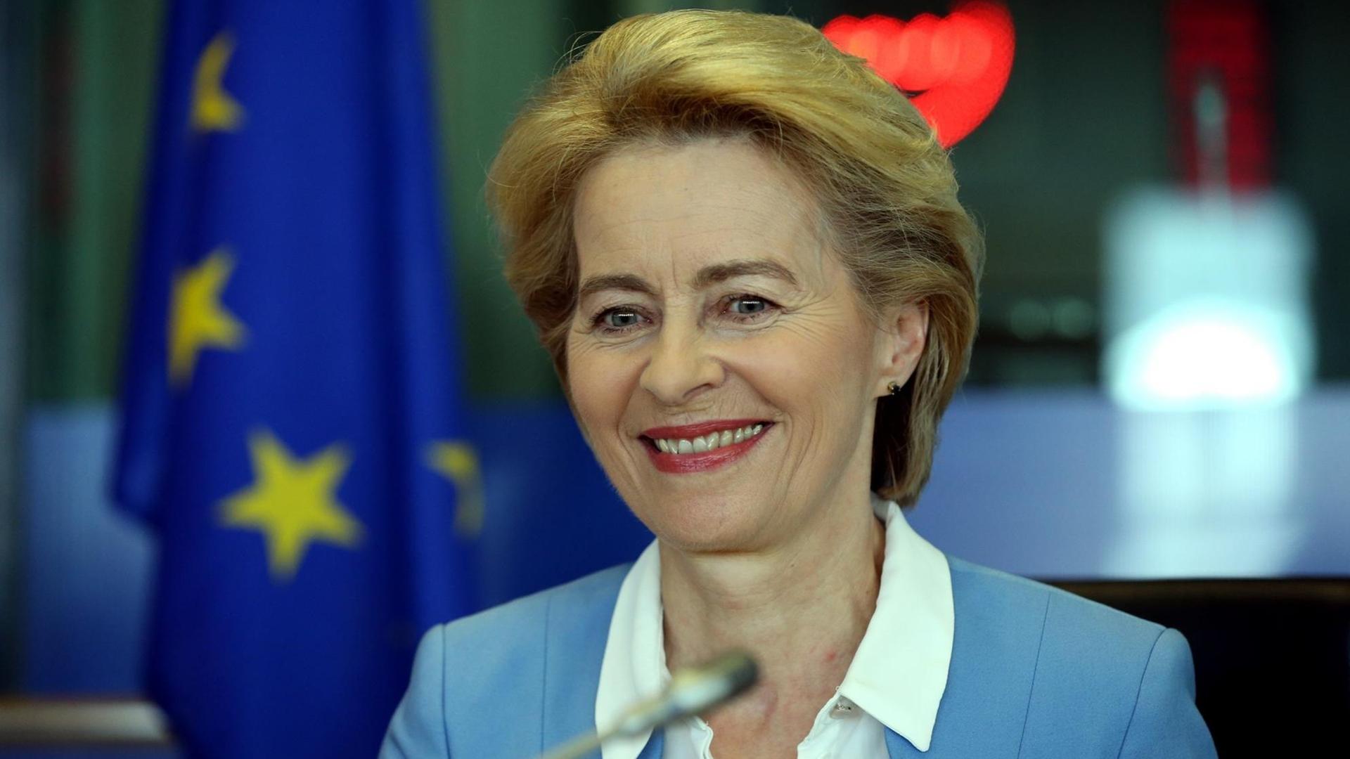 Bundesverteidigungsministerin Ursula von der Leyen (CDU) sitzt lächelnd vor einem Mikrofon bei ihrem Besuch in Brüssel