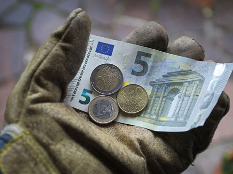 Eine Hand in einem Arbeitshandschuh hält acht Euro und fünfzig Cent.