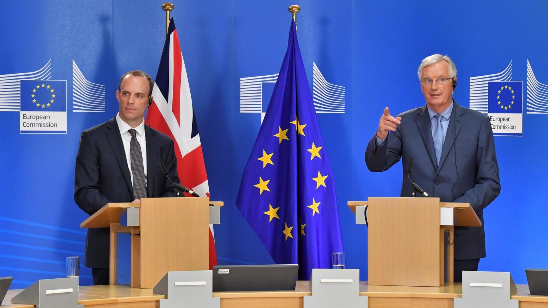 Das Bild zeigt den britischen Brexit-Unterhändler Dominic Raab (l) und EU-Chefunterhändler Michel Barnier (r). Sie halten gemeinsam im Gebäude der Europäischen Kommission eine Pressekonferenz ab. Sie stehen an hölzernen Pulten hinter Mikrofonen. Im Hintergrund sind eine britische und eine EU-Flagge zu sehen.