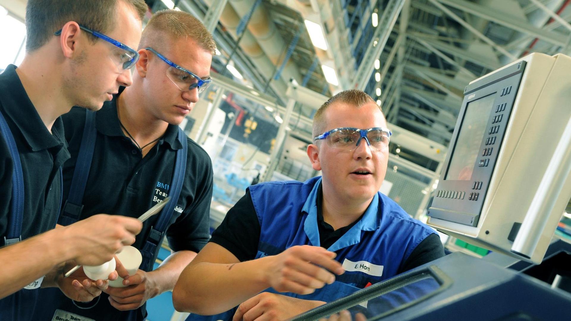 Im BMW-Werk in Leipzig erklärt der Ausbilder für Industrie-und Fertigungsmechaniker Enrico Horn (r) den angehenden Fertigungsmechanikern Henry Lange (l) und Chris Themel an einer CNC-Drehmaschine die Fertigung von Kunsthülsen.