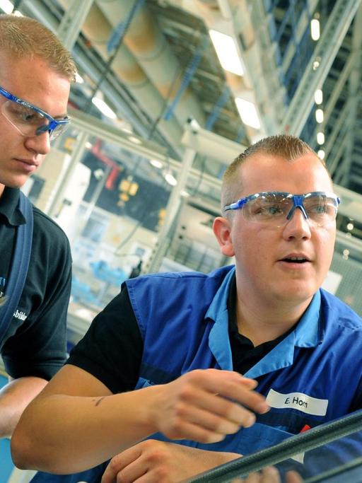Im BMW-Werk in Leipzig erklärt der Ausbilder für Industrie-und Fertigungsmechaniker Enrico Horn (r) den angehenden Fertigungsmechanikern Henry Lange (l) und Chris Themel an einer CNC-Drehmaschine die Fertigung von Kunsthülsen.