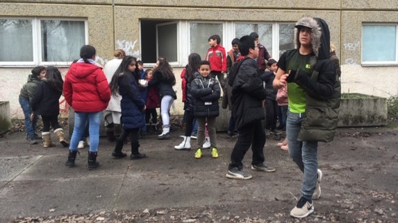 Kinder während der Schulpause vor einem tristen Gebäude.