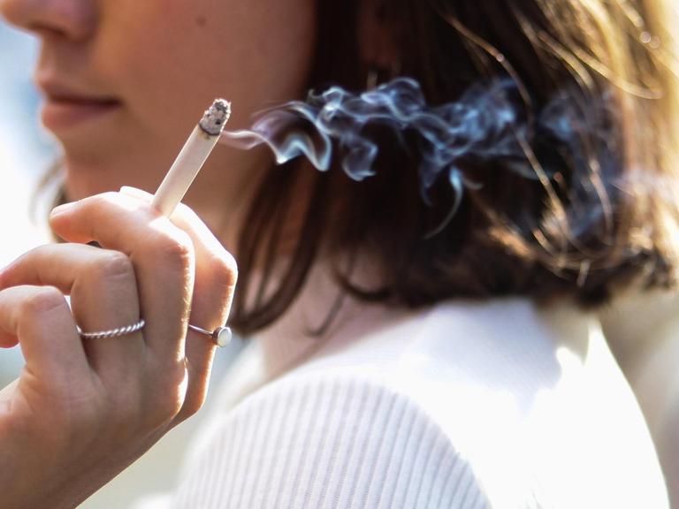 Eine junge Frau sitzt auf der Terrasse eines Cafes und raucht eine Zigarette.