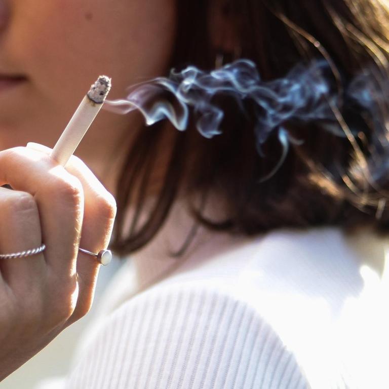 Eine junge Frau sitzt auf der Terrasse eines Cafes und raucht eine Zigarette.