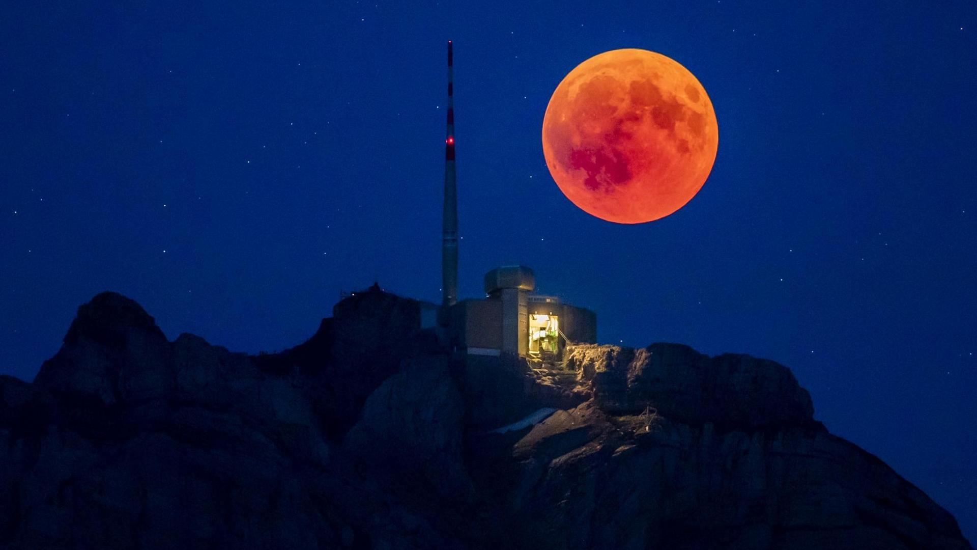 Rot steigt der Vollmond hinter dem Berg Säntis im Kanton Appenzell in der Schweiz auf.