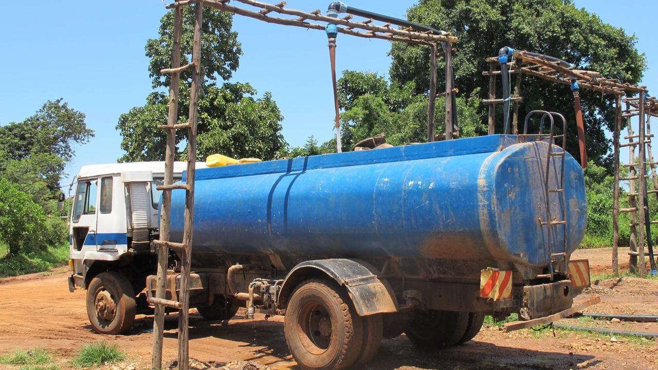 In einen alten LKW wird Wasser gefüllt. Der LKW steht im Staub unter einem Holztor.