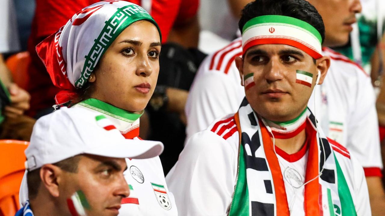 Mehrere Fußballfans in einem Fußballstadion. Sie tragen Fankleidung in den Landesfarben des Iran.