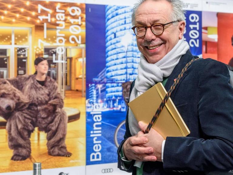 Dieter Kosslick verlässt das Podium der Pressekonferenz und blickt freundlich in die Kamera, während er eine graue Berlinaletasche schultert.