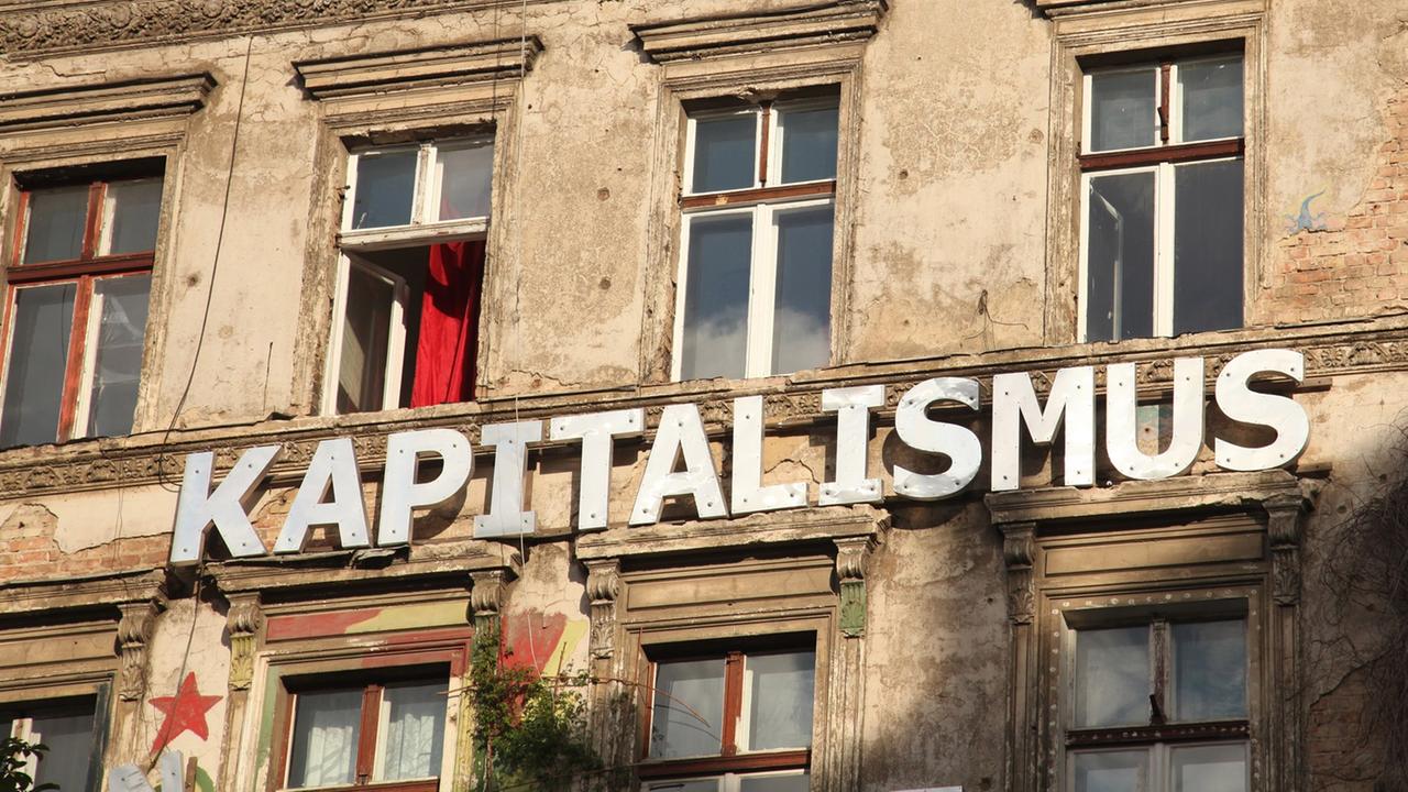 "Kapitalismus" steht auf einer Wand an einem besetzten Haus in einer Straße in Berlin im Stadtteil Prenzlauer Berg