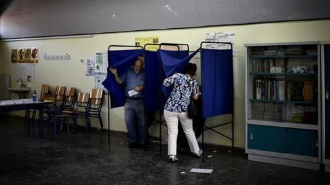 Zu sehen sind Menschen an einer Wahlurne in Athen.