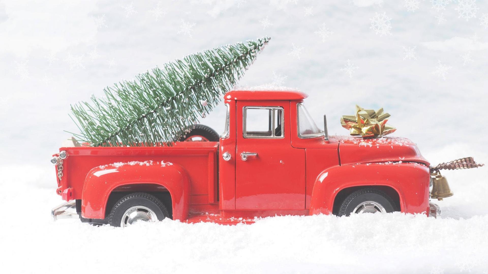Ein Modell-Pickup-Truck im Schnee mit Weihnachtsbaum auf der Ladefläche