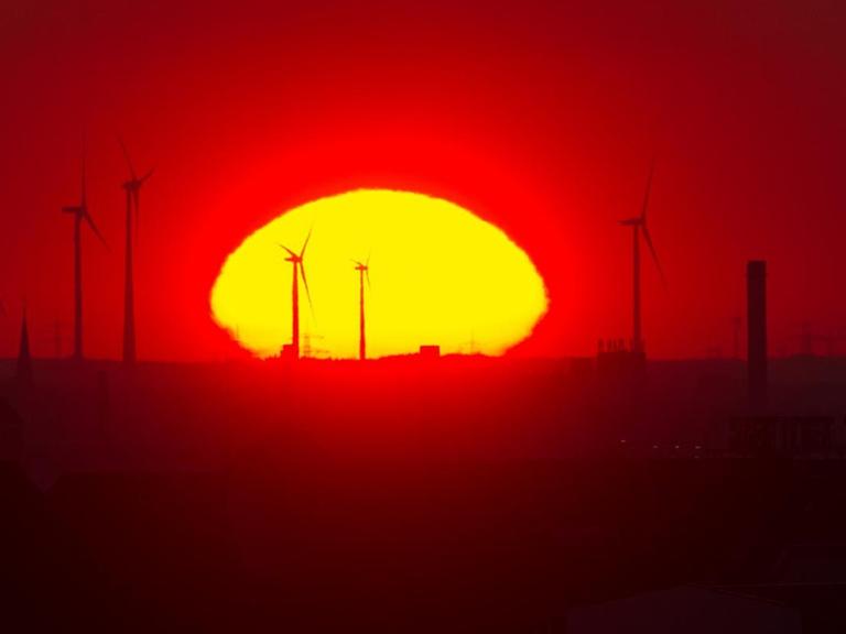 Die Sonne geht in Berlin hinter Windrädern nahe dem Autobahndreieck Pankow auf.