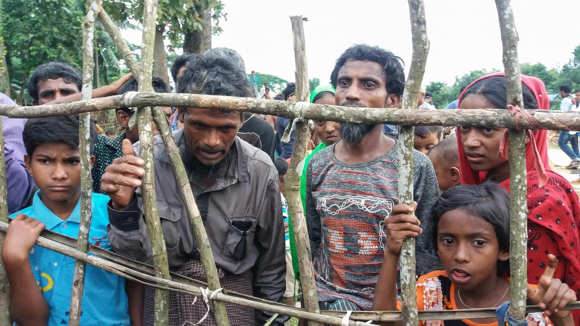 Rohingya-Flüchtlinge stehen hinter einem Holzzaun.