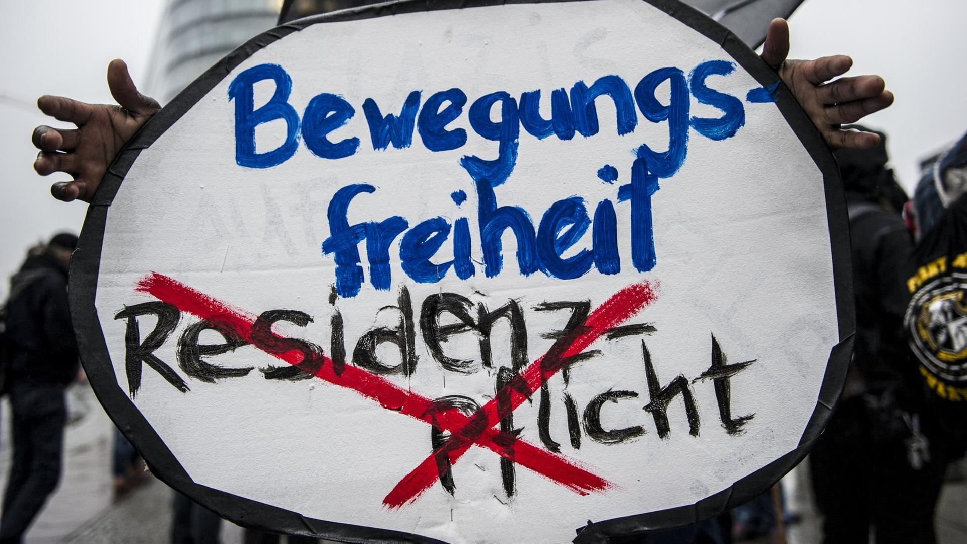 Auf einem Schild bei einer Demonstration steht der Schriftzug: "Bewegungsfreiheit", darunter, rot durchgestrichen: "Residenzpflicht".