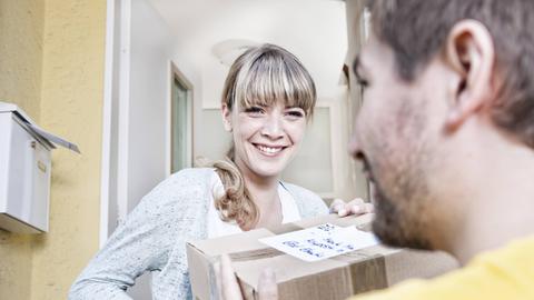 Eine junge Frau nimmt an der Haustür ein Paket von einem Paketboten entgegen.