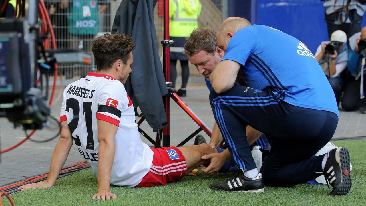 Der beim Torjubel im Spiel gegen den FC Augsburg verletzte HSV-Star Nicolai Mueller wird von Teamarzt Dr. Goetz Welsch und Physiotherapeut Uwe Schellhammer behandelt.