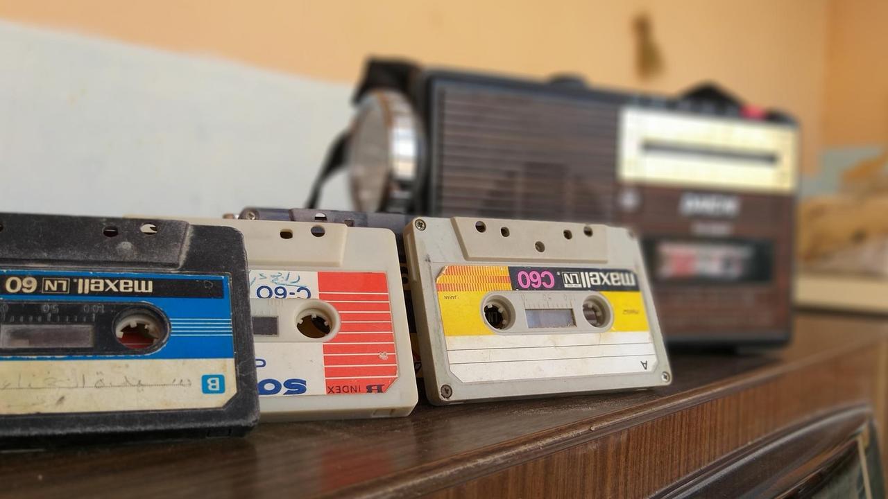 Drei Audiokassetten mit bunten Etiketten lehnen an einem alten Kassettenrecorder.
