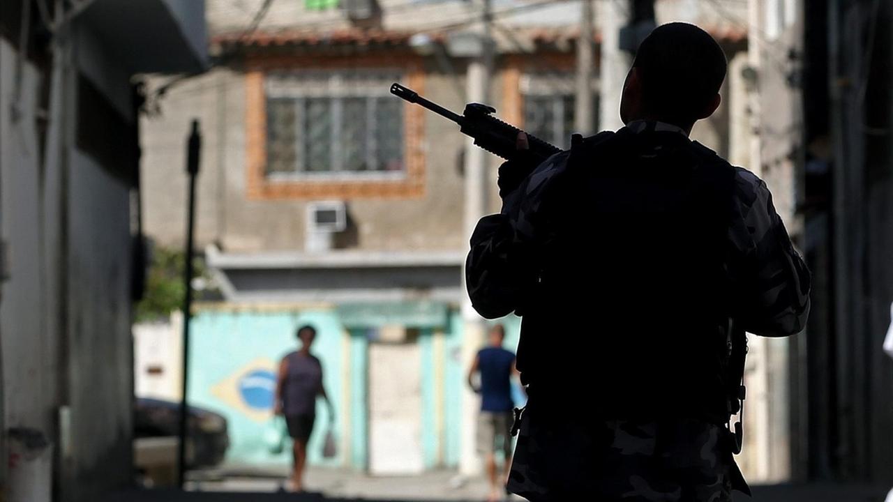 Ein Polizist mit Maschinenpistole im Anschlag steht in einer schmalen Gasse von Rio.