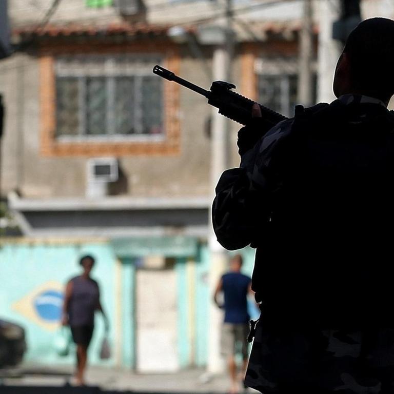 Ein Polizist mit Maschinenpistole im Anschlag steht in einer schmalen Gasse von Rio.