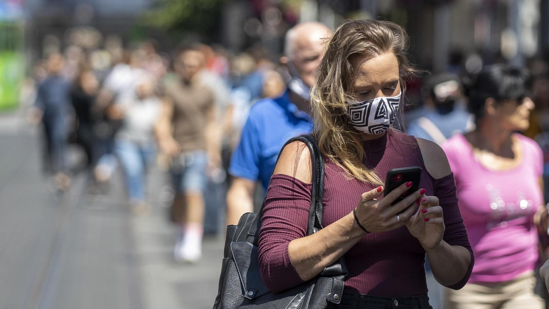 Eine junge Frau mit Mundschutz schaut auf ihr Handy.