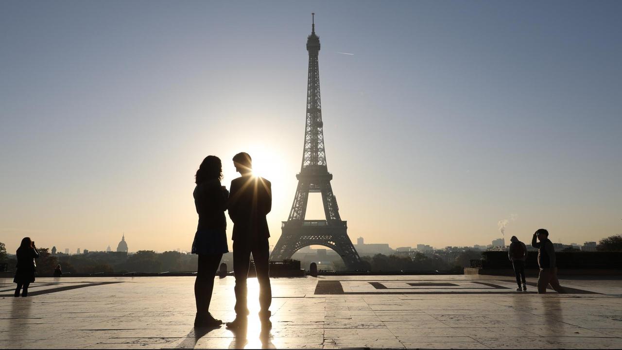 Menschen schauen sich vom Trocadero in Paris aus den Sonnenaufgang am Eiffelturm an.