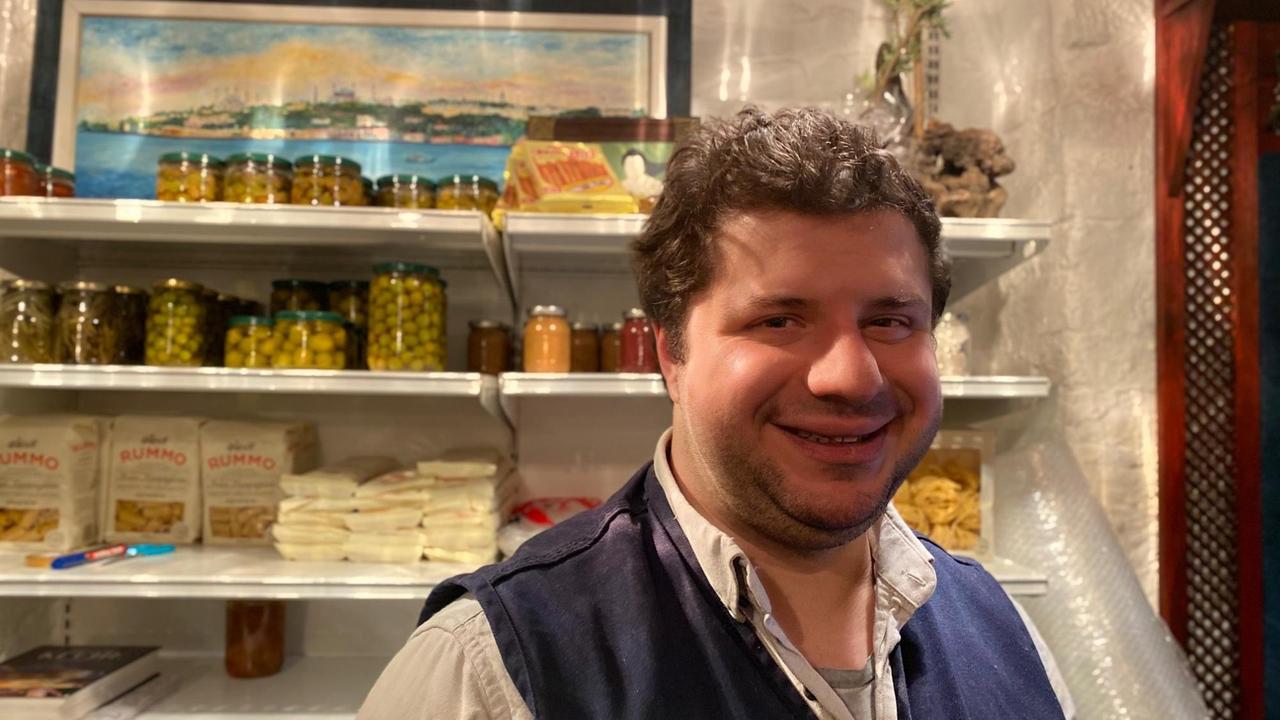 Ein rundlicher Mann steht lächelnd vor einem Lebensmittelregal.