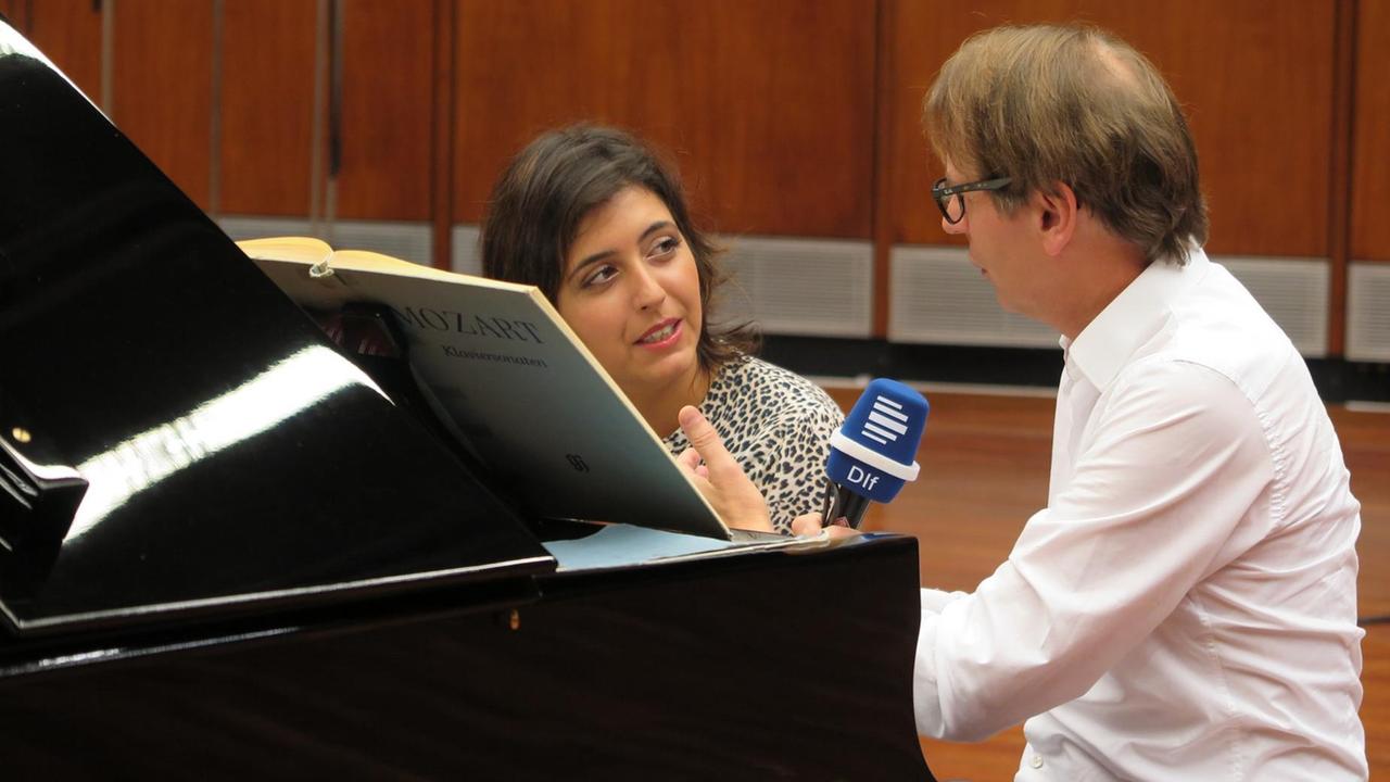 Eine Pianistin und ein Moderator sitzen an einem Flügel in einem Konzertsaal und sprechen miteinander.