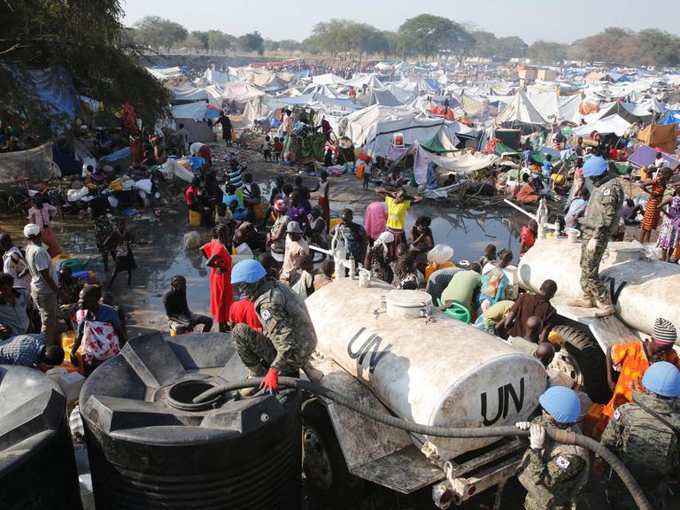 In einem Flüchtlingscamp mit zahlreichen Zelten werden Wassertanks durch Soldaten befüllt.