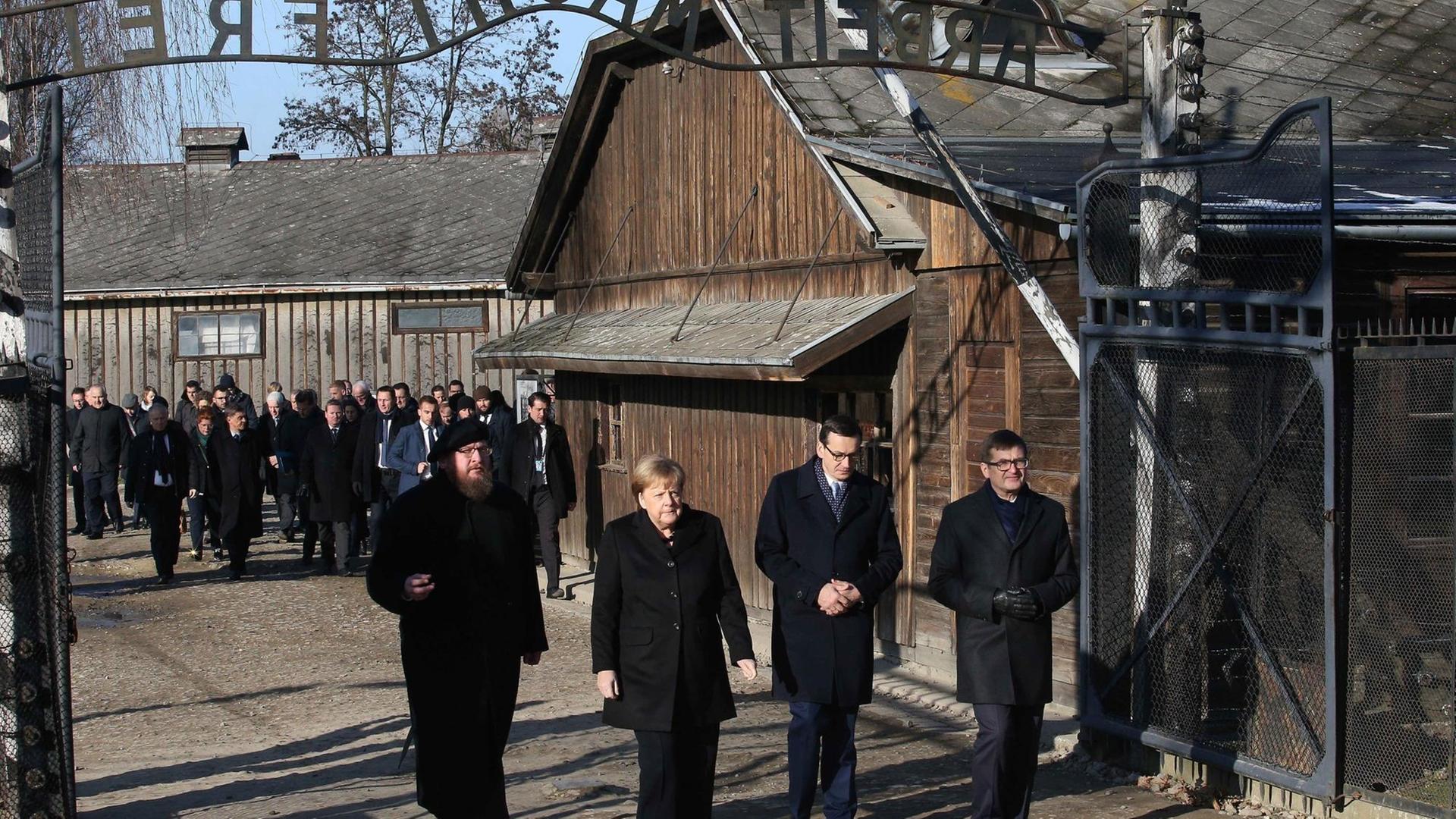 Angela Merkel geht mit ihren Gast-Gebern durch einen Eingang von Auschwitz.