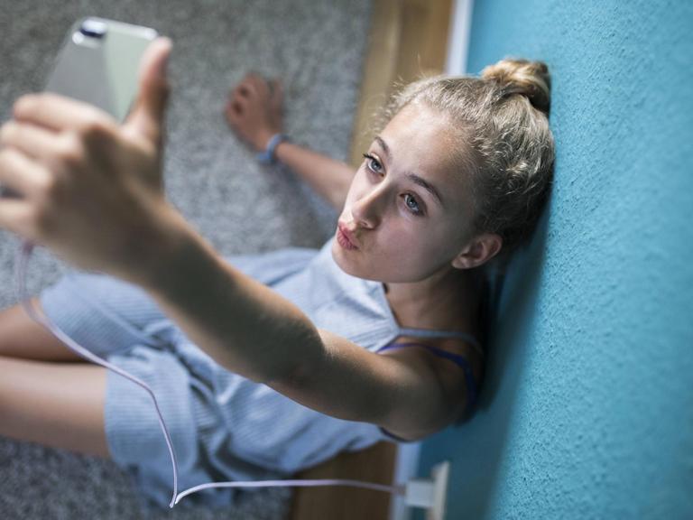 Ein Mädchen sitzt in seinem Zimmer auf dem Boden und macht Selfies.