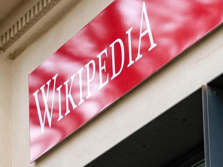Ein rotes Schild mit der weißen Aufschrift "Wikipedia" über einem Ladenlokal.