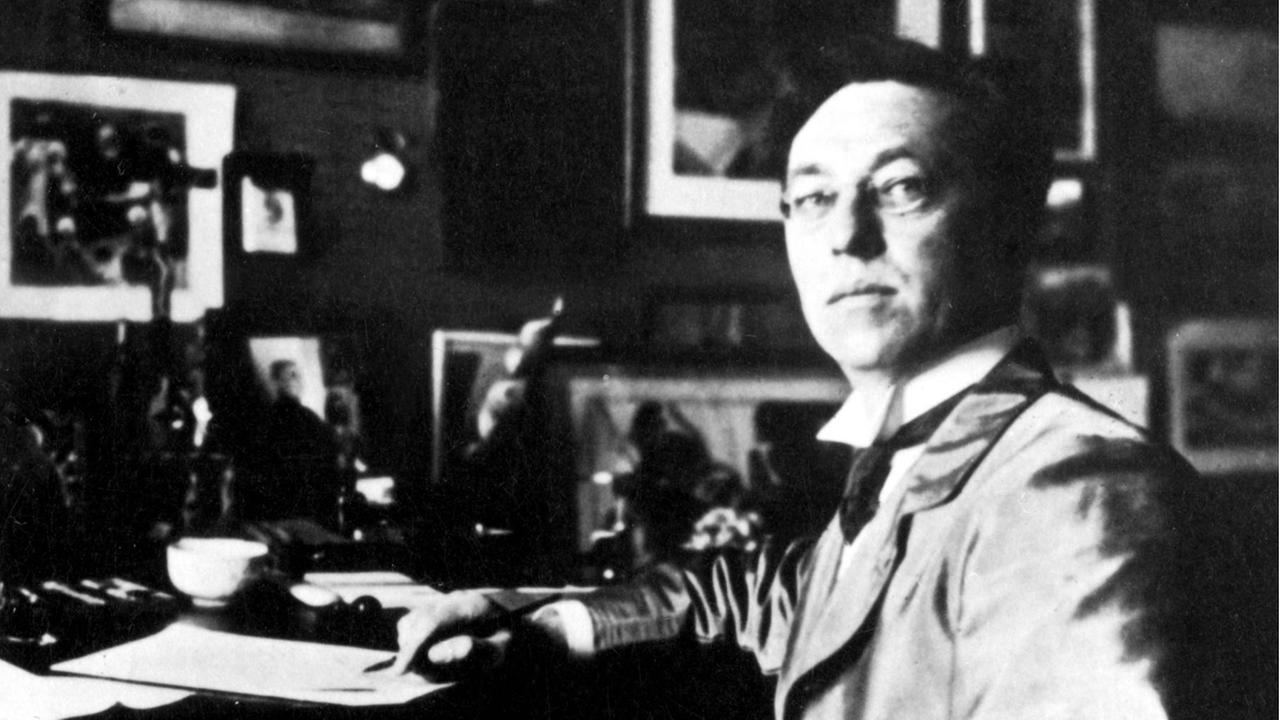 Historisches Foto des Malers Wassily Kandinsk, der an seinem Schreibtisch sitzt und über die Schulter in die Kamera schaut. Historisches Foto des Malers Wassily Kandinsk, der an seinem Schreibtisch sitzt und über die Schulter in die Kamera schaut.