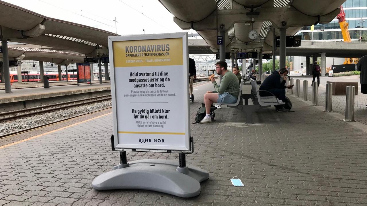 Neben den Bahnhofsgleisen steht am Bahnsteig ein großes gerahmtes Plakat mit Warnhinweisen.