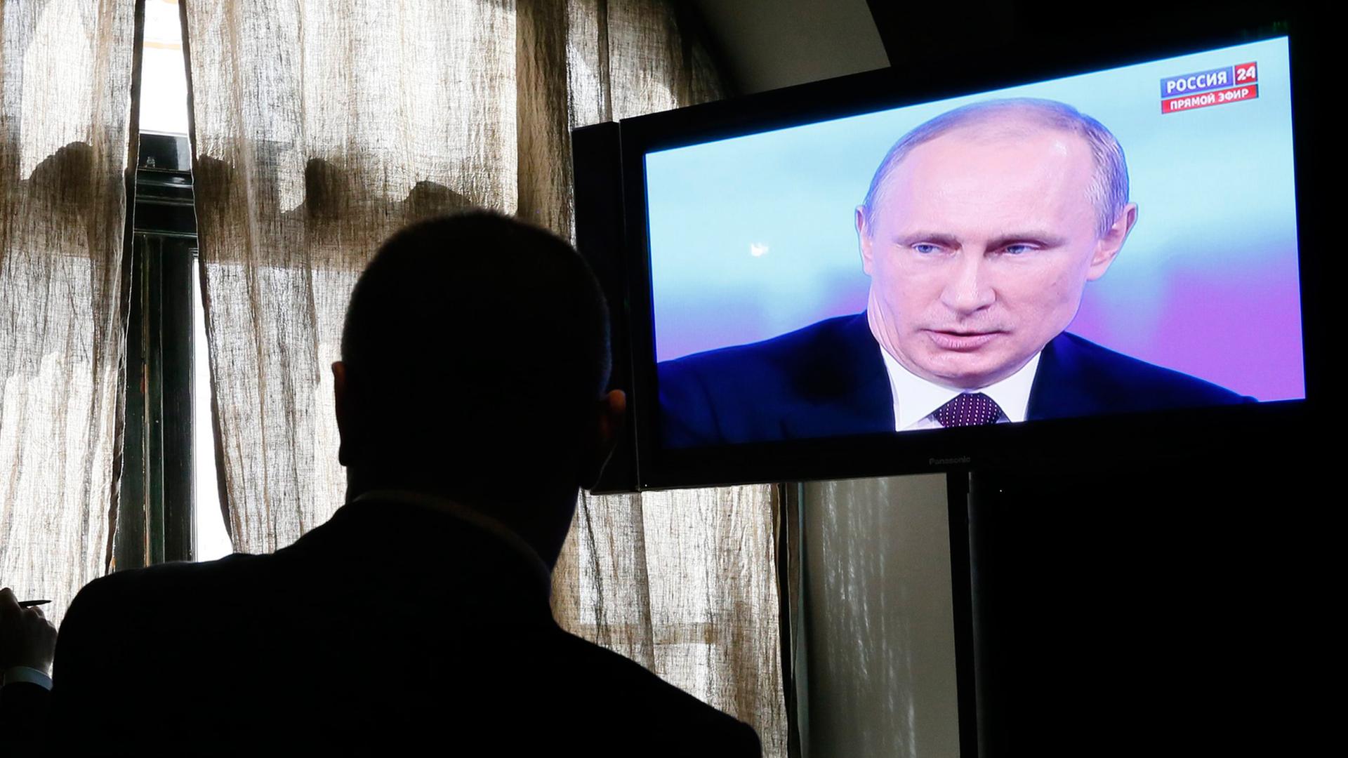 Ein Bildschirm zeigt die Fernsehsendung mit Wladimir Putin, davor als Schatten ein Zuschauer