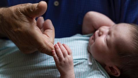 Ein neugeborenes Baby hält mit seiner kleinen Hand den Finger eines Grossvaters.