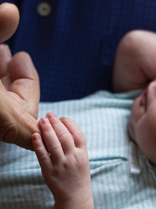 Ein neugeborenes Baby hält mit seiner kleinen Hand den Finger eines Grossvaters.